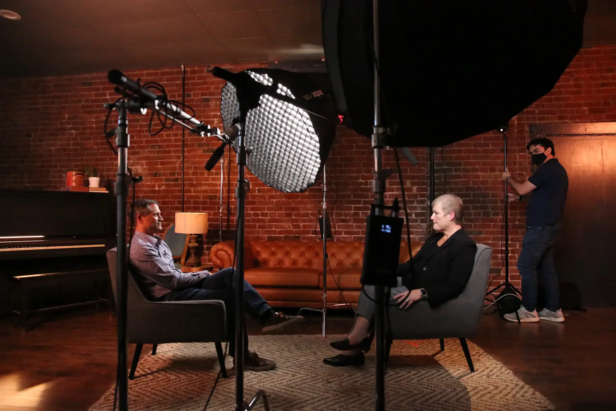 Two people seated for a filmed interview under studio lights