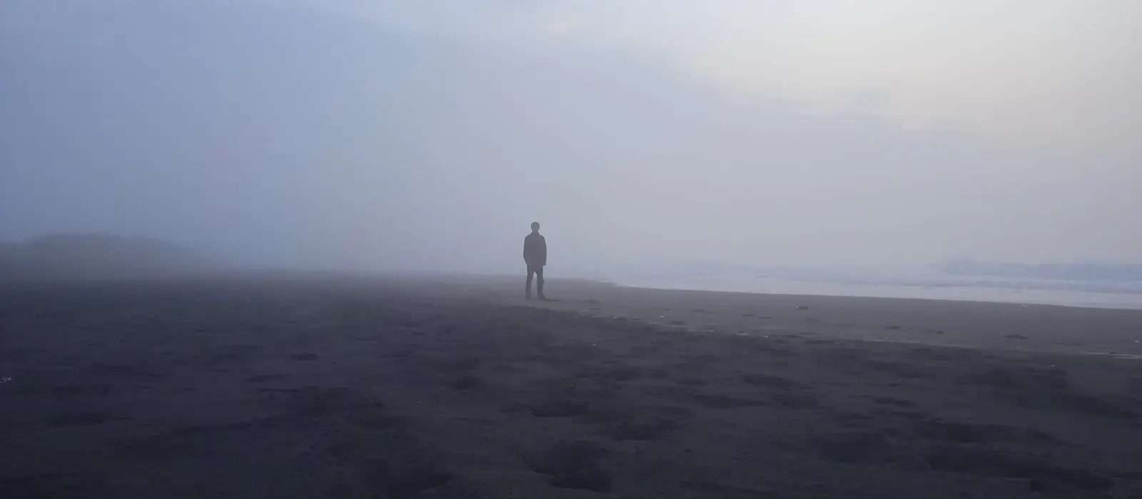 Film still: a lone figure on a fog-covered shore